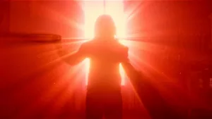 Une silhouette de jeune femme, vue de dos, illuminée par une lumière rouge intense, venant de la fenêtre devant elle, dans le film Traquée.