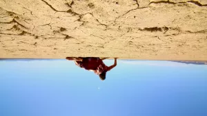 Un homme est allongé sur le sol craquelé du désert américain, sous un ciel bleu intense ; plan vu à l'envers du film The Outwaters.