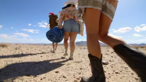 Plan fisheye sur les jambes de trois jeunes femmes arpentant le désert, en short et en bottes, dans le film The Outwaters.