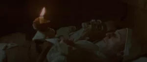 Un homme allongé dans son lit, une petite bougie dans la main, s'éveille à côté d'un cadavre squelettique dans Le Vourdalak, réalisé par Adrien Beau. 