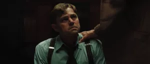 Leonardo Di Caprio assis dans la pénombre, les mains ligotées dans le dos, au bord des larmes ; une main d'homme inconnue est posée sur son épaule ; scène de Killers of the flower moon de Martin Scorsese.