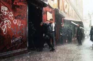 Brad Pitt et des agents de police s'apprêtent à entrer dans un bâtiment taggé, sous une pluie battante, dans le film Seven de David Fincher.