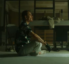 Michael Fassbender en position du lotus, vu de profil, sur un tapis de yoga, dans un appartement désaffecté ; plan issu du film The Killer.