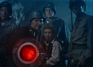 Quatre militaires dans une grotte, entourent un petit garçon qui dirige un faisceau rouge vers une cible hors-champ ; scène du film Les Envahisseurs de la planète rouge.
