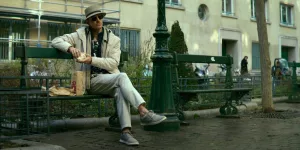 Michael Fassbender, déguisé en touriste allemand, assis sur un banc parisien comme si de rien n'était, les jambes croisées, à côté d'un sac Macdonald's, dans le film The Killer.