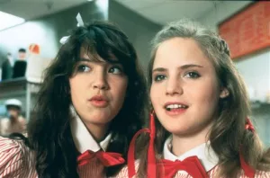 Jennifer Jason Leigh et Phoebe Cates en costume de serveuses dans le restaurant où elles travaillent, se parlent à l'oreille l'une de l'autre, en regardant devant elles, l'air malicieux, scène du film Ça chauffe au lycée Ridgemont.