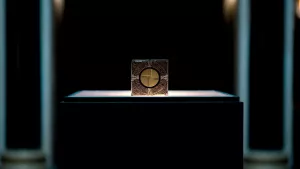 Le cube de Hellraiser (2022) donnant accès aux autres dimensions, posé sur un bloc noir, dans une galerie déserte et sombre.