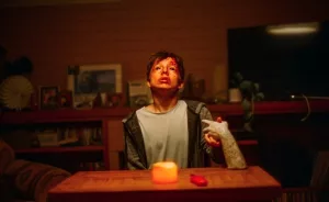 Un petit garçon semble possédé, assis à une table éclairée par une unique bougie, il lève le visage en l'air ; sur la table, une main qui tient la sienne ; plan du film La main.