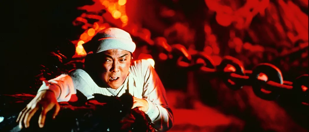 Un homme lutte pour ne pas tomber dans une grotte illuminée de rouge, comme si de la lave arpentait les murs, dans le film Zu les guerriers de la montagne magique.