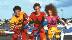 Les trois bikers en tenue fluo du film BMX Bandits posent fièrement, tout souriants, devant un port.