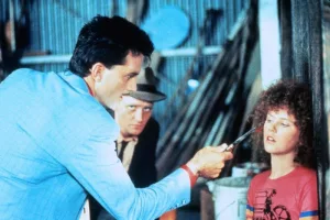 La très jeune Nicole Kidman séquestrée sous la menace d'un gangster qui la menace d'un couteau, dans un hangar en bord de mer ; scène du film BMX Bandits.