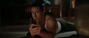 Bruce Willis à l'affût, allongé par terre, un revolver dans la main dans le film Die Hard : Piège de Cristal.