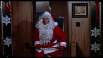 Le tueur jeune homme du film Douce nuit, sanglante nuit entre dans une pièce de maison toute en bois, décorée pour Noël, la fausse barbe baissée et la hache dans ses deux mains.