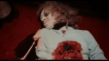 Une femme zombie git sur le sol rouge, un trou ensanglanté au niveau du thorax, dans le film Réveillon Sanglant.