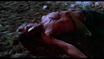 Un homme torse nu, mort, une grande lame lui traversant le ventre, gît sur une pelouse ; scène de nuit dans le film Douce nuit, sanglante nuit.