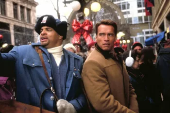 Dans une rue bondée à Noël, Schwarzenegger écoute la mine renfrognée les conseils d'un homme dans son dos, déterminé à lui montrer quelque chose ; scène du film La course aux jouets.