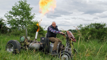 Un homme qui semble être un agriculteur pose dans une prairie au guidon de son étrange quatre roues, fait de produits de récupération, et qui dégage une grande flamme, dans le film Stéphane.