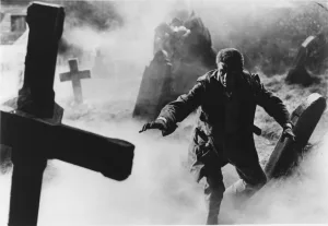 Un homme avance à tâtons dans un cimetière aux croix de travers et plongé dans une brume épaisse ; plan du film Horror Hotel.