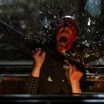 Vu du dessus un homme en sang est expulsé d'une fenêtre qui vole en éclats, dans le film Le jour de la bête.