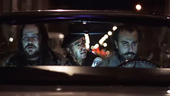 Les trois héros du film Le jour de la bête sont dans une voiture ; le prêtre au visage ensanglanté sur la banquette arrière essaie de plaider pour sa cause auprès des deux malfrats devant, déterminés.