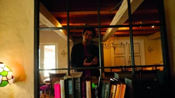 Bastien Garcia se filme dans le miroir au dessus d'une étagère de livre, dans un beau salon avec des poutres au mur ; plan extrait du film Stéphane.