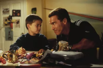 Howard Langston (Arnold Schwarzeneggger) taquine son fils pendant que ce dernier dessine à la table de sa chambre dans le film La course aux jouets.