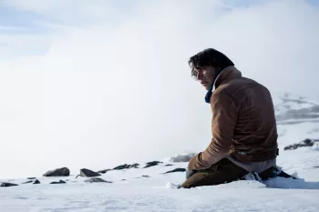 Un homme, abattu, vu de dos, est assis sur la neige dans un environnement désert, dans Le Cercle des Neiges de Juan Antonio Bayona.