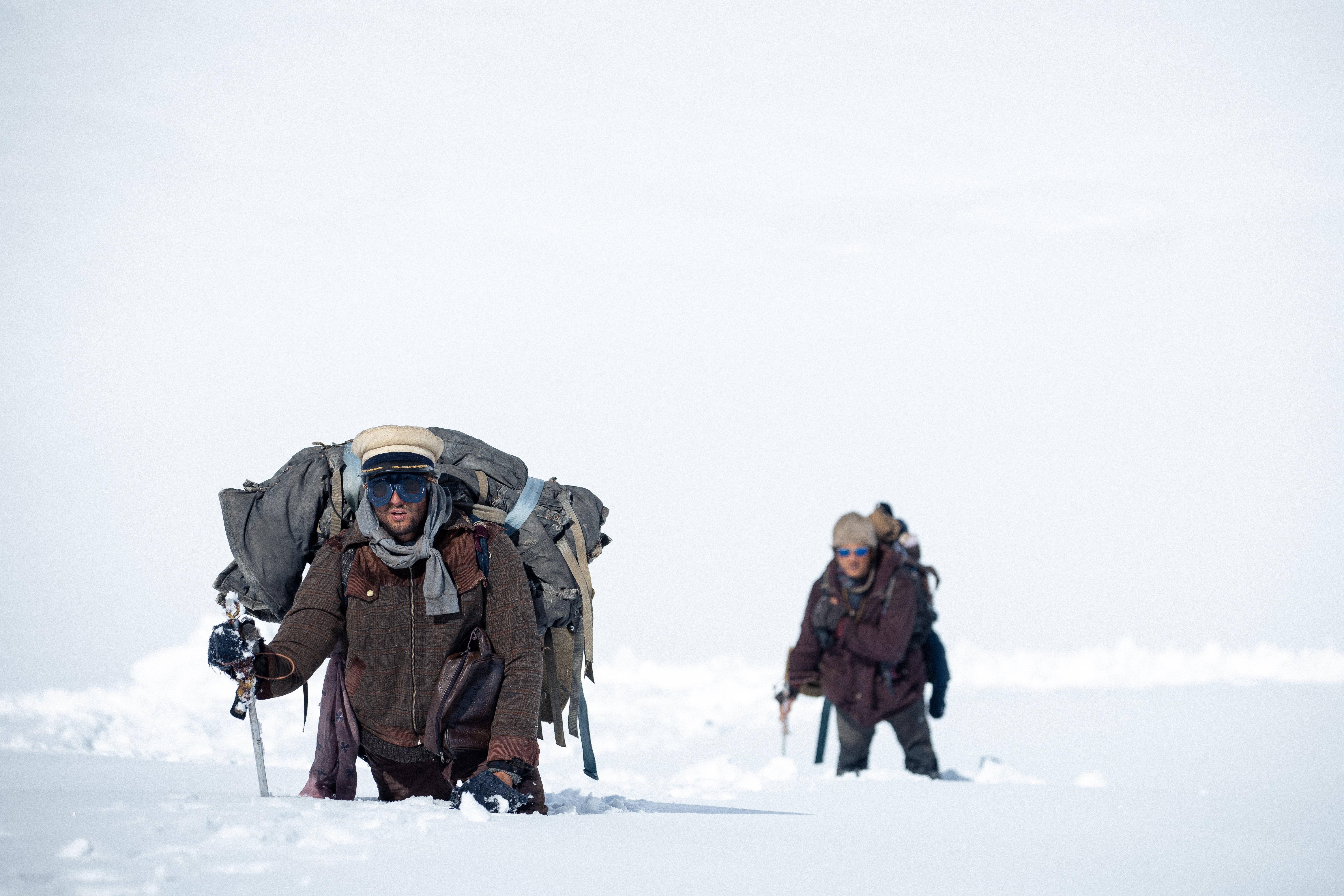 Deux hommes, en combinaison de grand froid, avec lunettes et paquetage sur le dos, tentent de progresser avec difficulté dans un amas de neige désertique ; scène du film Le cercle des neiges.