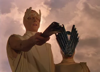 Un homme avec une cape style Antique, et un couvre-chef en forme de feuille tout auteur du crâne tend un parchemin devant lui dans le film Chroniques Martiennes.
