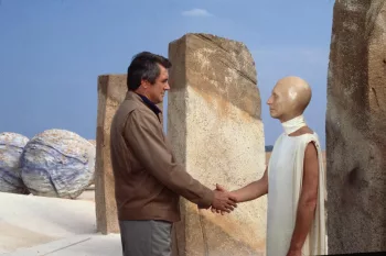 Au milieu de stèles de couleur sable, Rock Hudson serre la main d'un extraterrestre, humanoïde au visage comme de la cire, et portant une toge blanche ; plan issu des Chroniques martiennes.