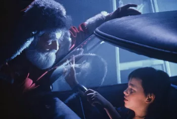 Le Père Noël de 3615 code Père Noël de René Manzor se penche sur le parebrise d'une voiture, s'adressant au petit garçon assis sur le siège conducteur.