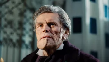 Plan rapproché-épaule sur Willem Dafoe, dont le visage semble avoir été recomposé d'après différentes fragments de peaux, dans le film Pauvres créatures.