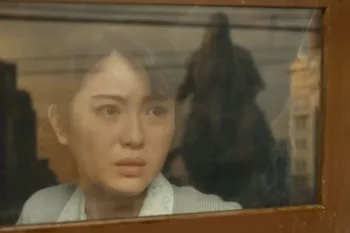 Une jeune femme au regard inquiet, regarde dans le train, voit Godzilla s'approcher d'elle, dont on voit le reflet sur la vitre ; plan issu du film Godzilla Minus One.
