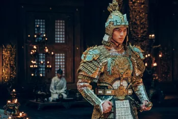 Le Prince Yin Shou en armure serre les poings, déterminé, dans une pièce de son palais ; derrière lui un laquais tout de blanc vêtu, est à genoux ; scène du film Creation of the Gods I: Kingdom of Storms.