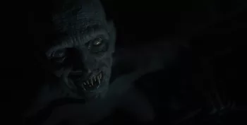 Gros plan sur le visage monstrueux, chauve avec des dents crochues et des yeux gris, de Dracula dans la pénombre du film Le dernier voyage du Demeter.