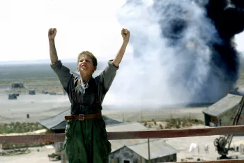 Un jeune garçon en tenue militaire lève les bras au ciel tandis que derrière lui une fumée d'explosion se lève vers le ciel ; extrait du film L'Empire du soleil de Steven Spielberg, sujet du livre écrit par le Cinématographeur.