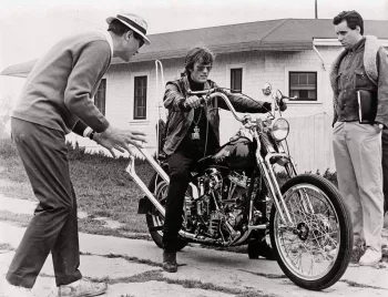 Peter Fonda sur sa moto, devant une petite maison américaine, sous le regard de Roger Corman qui lui donne des intentions jeu (photo en noir et blanc).