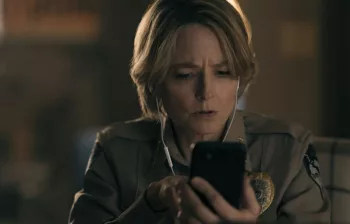 Jodie Foster en tenue de shériff consulte son téléphone portable, surprise et inquiète dans la série True Detective : Night COuntry.