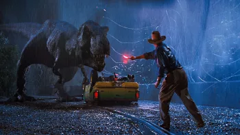 Sam Neill essaie d'écarter le T-Rex de sa voiture retournée sur le goudron avec une fusée éclairante ; scène sous la pluie de Jurassic Park de Steven Spielberg.