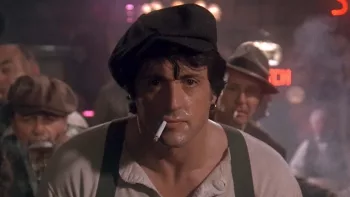 Plan rapproché-épaule, de face, sur Sylvester Stallone dans le film La taverne de l'enfer : la cigarette au bec, il est dans un bar, peuplé, en sueur, vêtu comme un jeune homme du début du siècle, et son regard va devant lui, à la fois déterminé et un peu absent.