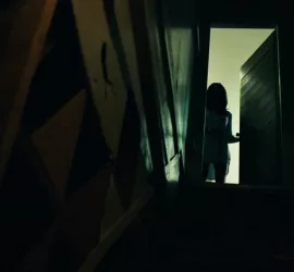 En contre-plongée, la silhouette d'une femme, peu éclairée, observe un sous-sol du haut de l'escalier qui y mène ; scène du film Fear de Deon Taylor.