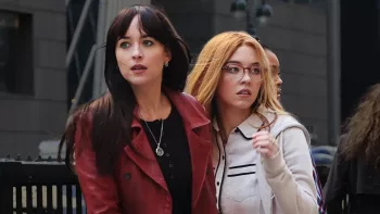 Dakota Johnson guide Sydney Sweenie à travers une foule de badauds observant quelque chose, toutes les deux alertes, dans le film Madame Web.