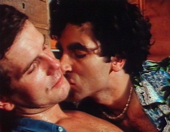 Un homme embrasse sur la joue un autre, qui ferme les yeux, dans les années 1970 ; plan issu du film X D'hommes à hommes.