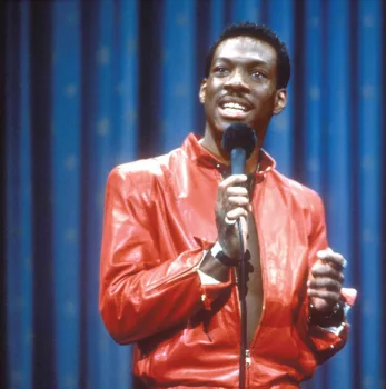 Le jeune Eddie Murphy sur scène, en stand-up, vêtu d'une veste de cuir rouge.