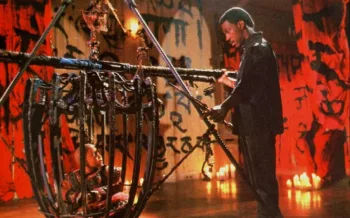 Eddie Murphy échange avec un enfant moine bouddhiste qui est enfermé dans une cage en bois ; le décor est une pièce vide dont les murs rouges et bois sont tapissés d'idéogrammes asiatiques ; plan issu du film Golden Child.