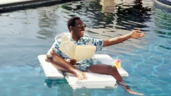 Eddie Murphy hilare dans une piscine, en chemise hawaïenne, assis sur une bouée.