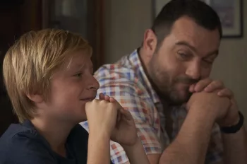 Denis Ménochet regarde son fils avec le sourire, tous deux assis côte à côte dans le film Jusqu'à la garde de Xavier Legrand.
