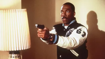 Scène du film Le flic de Beverly Hills 3 où Eddie Murphy, surpris, tient son pistolet à deux mains, prêt à tirer ; près de lui, une lampe qui projette son ombre sur le mur derrière lui.