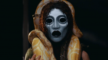 Plan rapproché-épaule sur une femme torse nu, aux cheveux mouillés, qui porte un masque blanc, les yeux et la bouche cerclés de noir profond ; un serpent file tout autour de son cou et de son crâne ; issu du long-métrage A Wounded Fawn.