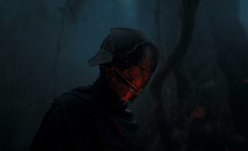 Un inquiétant Sith portant un casque sans yeux set tient debout au cœur d'une forêt angoissante, plongée dans le brouillard, avec de rares arbres fins ; plan issu de la série Star Wars The Acolyte sur Disney +.
